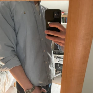 Blå skjorta från Ralph Lauren - Säljer en stilren blå skjorta från Ralph Lauren med klassisk krage och knappar framtill. Skjortan har långa ärmar och ett broderat märke på bröstet. Perfekt för en snygg och avslappnad look. Storleken är 18(s), och passar om man är upp till 180 skulle jag säga.