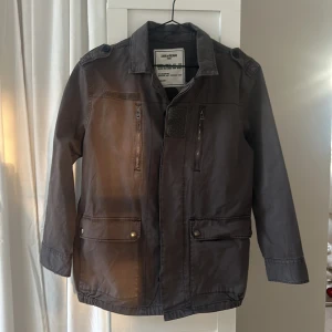 Grå jacka från Zadig & Voltaire - Cool grå jacka från Zadig & Voltaire med broderade detaljer på ryggen, inklusive blommor och fredssymbol. Jackan har dragkedja och knappar framtill samt flera praktiska fickor. Perfekt för en unik stil. Storleken 12y motsvarar Xs.