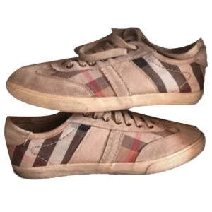 Burberry skor - Snygga beige sneakers från Burberry med klassiskt rutigt mönster i sidorna. Skorna har snörning och är tillverkade i skinn och syntetmaterial. Perfekta för en stilren look.