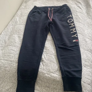 Svarta mjukisbyxor från Tommy Hilfiger - Snygga svarta mjukisbyxor från Tommy Hilfiger med logga längs benet. Byxorna har en bekväm passform med snörning i midjan och muddar vid bensluten. Perfekta för en avslappnad stil.