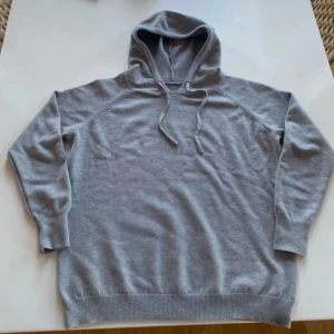 Merino hoodie - Säljer en stilren grå hoodie med långa ärmar och ribbade muddar. Perfekt för en avslappnad look. Den har en praktisk huva med dragsko för justering. Den är i skönt stickat material. Säljer för att den är för liten för mig. Alltså har den inge problem och är helt ny.