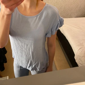 Ljusblå topp från ICHI - Säljer en söt ljusblå topp från ICHI i storlek M. Den har korta ärmar med volangdetaljer och en rund halsringning. Perfekt för vår och sommar! 