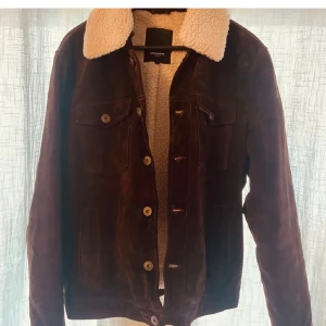 Brun mockajacka från Rockandblue - Säljer en snygg brun mockajacka från Rockandblue i storlek L. Jackan har en mysig vit pälsfodrad krage och knappar framtill. Perfekt för höst och vinter med sin varma och stiliga design. Passar både till vardags och fest!