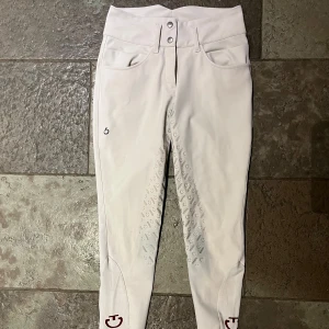 Vita ridbyxor från Cavalleria Toscana - Snygga vita tävlings ridbyxor från Cavalleria Toscana i högmidjad modell. De har en tight passform och är dekorerade med diskreta loggor längs benen. Byxorna har knappar i midjan och är gjorda i ett stretchigt material för bästa komfort. Svensk storlek 36 IT40 