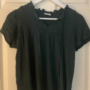 Grön blus/tröja - Säljer en söt grön blus med volangdetaljer vid halsen. Den har en v-ringad design och korta ärmar, perfekt till jul med en svart kjol. Passar både till vardags och festligare tillfällen. Skulle säga att storleken är mer åt 36. 
