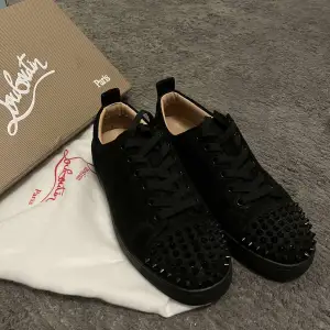 Säljer ett par svarta sneakers i mocka från Christian Louboutin. De har sina ikoniska nitar och den klassiska röda sulan. Skorna är i mycket bra skick och kommer med originalkartong och dustbag. Perfekta för att ge din outfit en fin touch, storlek 39 men passar även 40