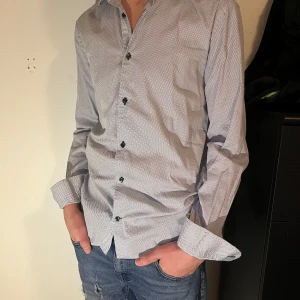 Vit och svart mönstrad skjorta - Snygg skjorta från Riley med små svarta prickar, perfekt för både vardag och fest. Jag är 1,80 lång och väger 70 kg. Skjortan är storlek M. 