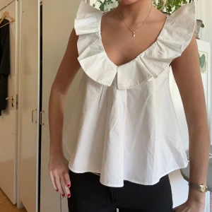 Vit Zara blus med volangdetaljer  - Säljer en superfin vit blus med volangdetaljer runt halsen. Den är ärmlös och har en luftig passform, perfekt för sommardagar. Blusen är i mycket bra skick och passar både till vardags och fest. Perfekt att matcha med jeans eller kjol!