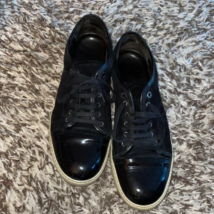 Svarta sneakers från Lanvin - Säljer ett par svarta sneakers från Lanvin i bra skick. Skorna har en glansig finish och klassisk snörning. De har en vit sula som visar lite användning men är fortfarande i gott skick.  Priset är ej hugget i sten och kan sänkas vid snabb affär!!
