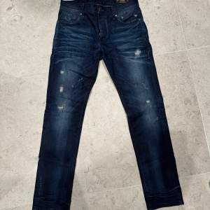 Säljer ett par marinblå Jack & Jones-jeans i storlek W30 L32, med trendiga slitningar för en modern look. Skick 9/10 – sparsamt använda och i fint skick. Hör gärna av dig om du har frågor eller vill veta mer!