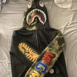 Svart och kamouflage hoodie från A Bathing Ape - Snygg hoodie från Bape, den är äkta med bra skick och utan defekter. Köpt på herr men passar lika bra till tjejer. Skriv om du har frågor.