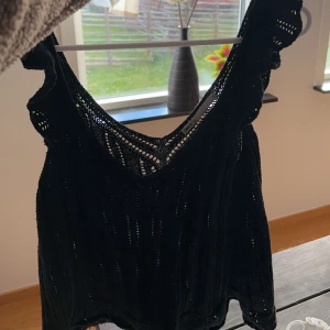 Svart ärmlös topp - Snygg svart ärmlös topp med spetsdetaljer. Perfekt för en sommarkväll eller fest. Den har en vacker öppen rygg och är gjord i ett lätt och luftigt material. Passar bra till både jeans och kjol.