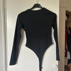 Svart långärmad bodysuit - Snygg svart långärmad bodysuit i ribbat material. Perfekt för både vardag och fest. Den har en tight passform som framhäver figuren och en stilren design som passar till allt. Ett måste i garderoben för alla säsonger!