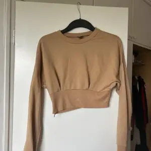 Säljer en snygg beige croppad tröja med långa ärmar. Perfekt för en avslappnad stil, den har ribbade muddar vid ärmslut och nederkant. Passar bra till både jeans och kjol. Perfekt för höst och vår!