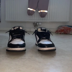 Pandas - Säljer ett par klassiska svartvita Nike sneakers i bra skick. De har en snygg och tidlös design med snörning och Nike-loggan tydligt synlig. Perfekta för vardagsbruk eller en avslappnad stil. Skorna är bekväma och passar till det mesta i garderoben.