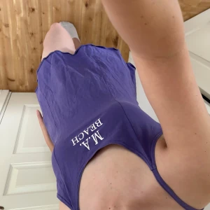 Lila strandklänning med tryck - Säljer en söt lila strandklänning med texten 'M.A. BEACH' på framsidan. Klänningen är ärmlös med smala axelband och har en avslappnad passform, perfekt för sommardagar på stranden. Y2K. 