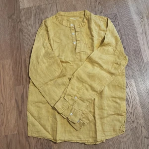 Gul linne henley-skjorta - Säljer en snygg gul henley-skjorta i linne. Perfekt för vår och sommar med sin lätta och luftiga känsla. Skjortan har långa ärmar och knappar framtill. Den är i bra skick och passar både till vardags och festligare tillfällen. Ett måste i garderoben för en stilren look! 🌼
