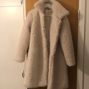 Beige teddyjacka - Säljer en supermysig beige teddyjacka i mycket bra skick. Perfekt för höst och vinter! Jackan är långärmad och gjord av 100% polyester, vilket gör den både varm och lätt att ta hand om. Den har en klassisk stil utan knappar eller dragkedja, vilket ger en avslappnad look. Perfekt för att hålla sig varm och stilren i kylan!