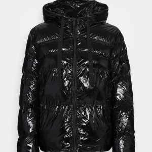 Svart glansig pufferjacka - Säljer en svart glansig pufferjacka med huva och dragkedja. Perfekt för kalla dagar med sin quiltade design som håller värmen. Jackan har en normal passform och långa ärmar, vilket gör den idealisk för både höst och vinter. Den är i mycket bra skick och redo för nya äventyr!