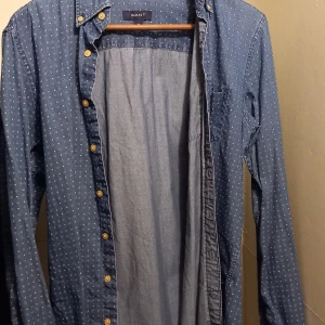 Blå mönstrad skjorta från GANT - Säljer en snygg blå skjorta från GANT i storlek M. Skjortan har ett diskret mönster och är långärmad med knappar. Perfekt för både vardag och festliga tillfällen. Materialet känns som bomull och ger en skön passform. Passar bra till både jeans och chinos!