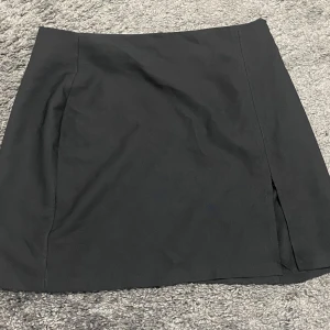 Svart kjol med dragkedja och slits - Snygg svart kortkjol i storlek L. Kjolen har en diskret dragkedja på sidan och en slits på sidan och är perfekt för både vardag och fest. Den är i mycket bra skick och passar utmärkt till höst- och våroutfits. Enkel att matcha med olika toppar och accessoarer.🖤/använd 1 gång 