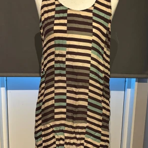 Randig klänning från Truly - Säljer en cool randig klänning från Truly i storlek L. Den har ett mönster med bruna, beige och gröna ränder. Perfekt för en avslappnad sommarlook. Klänningen är ärmlös och har en bekväm passform.