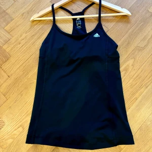 Svart linnetopp från Adidas - Säljer en svart linnetopp från Adidas i storlek XS. Nästan helny! Snygg med smala axelband. Passar perfekt för gymmet eller löprundan!