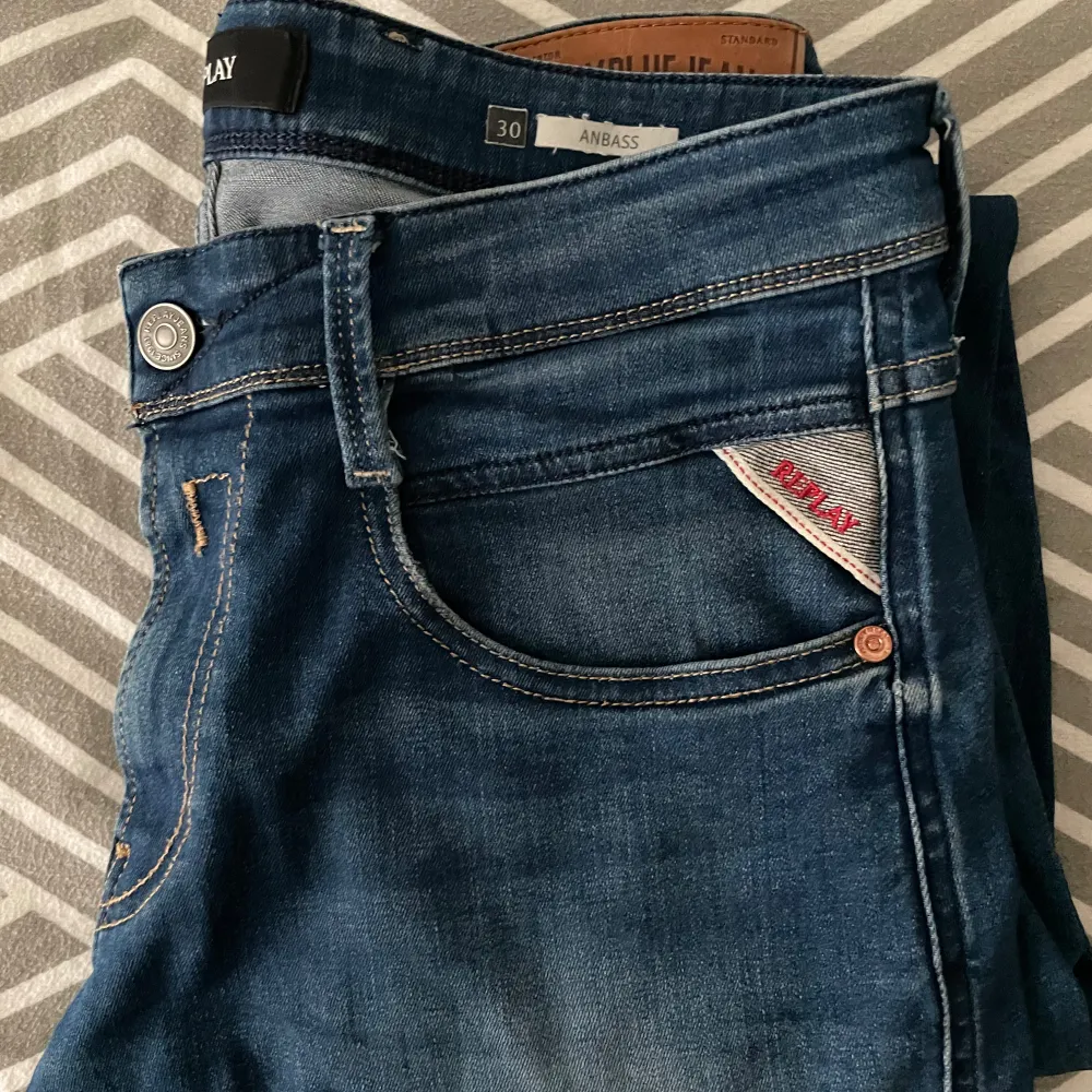 Säljer ett par snygga blå jeans från Replay Anbass. De har en klassisk femficksdesign med knapp och dragkedja. Jeansen är i bra skick och har en normal passform. Perfekta för både vardag och fest!. Jeans & Byxor.