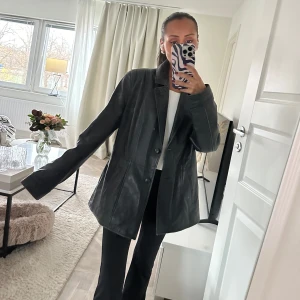 Svart skinnjacka äkta läder - Säljer en snygg svart skinnjacka i äkta läder vintage. Jackan har en klassisk design med knappar framtill och långa ärmar. Perfekt för höst och vår, och ger en stilren look till vilken outfit som helst. Använd ett fåtal gånger, så den är i mycket bra skick. Passar både till vardags och fest! Köpt i Spanien i en läderbutik för 1600kr.