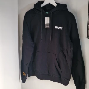 Svart hoodie från Montana Cans - Säljer en svart hoodie från Montana Cans i storlek M. Den är helt ny och har en stilrenl logga på bröstet och små detaljer som gör den unik. Se bild. Perfekt för höst och vinter med sin mysiga känsla. Den har en klassisk känguruficka och ribbade muddar. Grym för både chill och streetwear! 🖤