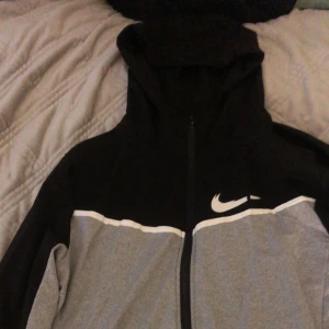 Svart och grå hoodie från Nike - Säljer en snygg och bekväm svart och grå hoodie från Nike. Den har en dragkedja framtill och den klassiska Nike-loggan på bröstet. Perfekt för både träning och vardag!