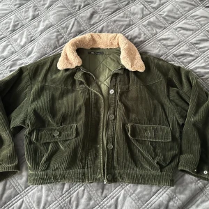 Olivgrön manchesterjacka från ONLY - Säljer en superfin olivgrön manchesterjacka från ONLY. Den har en mysig beige fuskpäls på kragen och stängs med knappar. Pälsen är avtagbar.  Jackan har två stora fickor framtill,kortare modell med avslappnat form och är perfekt för höst och vår. Den är i storlek dam 38 ( herr strl S)och är i bra skick. Perfekt för att hålla stilen nu när det blir lite kyligare ute!