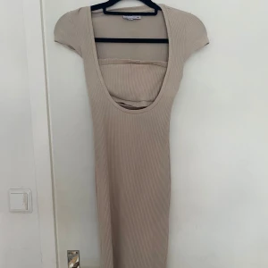 Beige ribbad klänning - Säljer en superfin beige ribbad klänning med korta ärmar och en snygg slits på sidan. Den har en djup, rundad urringning som ger en chic look, den i mitten ska vara som en liten tub topp som är kopplad till klänningen vilket gör det så fint. Perfekt för både vardag och fest! Storlek XS, PRIS KAN DISKUTERAS!