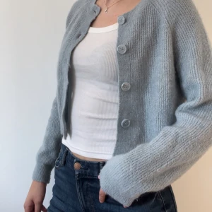 Ljusblå stickad kofta - Säljer en superfin ljusblå stickad kofta med stora knappar framtill. Den är croppad och har långa ärmar, perfekt för både vår och höst. Koftan är i ett mjukt och bekvämt material. Är i storlek M men sitter som en S