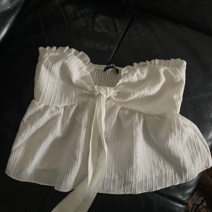 Vit topp från SHEIN - Säljer en superfin vit topp från SHEIN i storlek XS. Den är ärmlös och har en söt knytning framtill som ger en romantisk touch. Perfekt för sommardagar eller en festlig kväll. Materialet är lätt och luftigt, vilket gör den bekväm att bära. Toppen är i jättebra skick och aldrig använd!