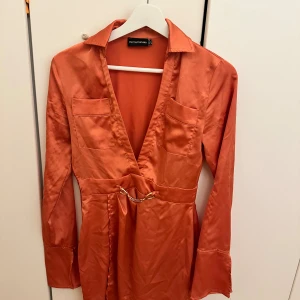 Coral rosa klänning i glansigt material - Festlig klänning i glansigt material från  Pretty Little Thing. Formar kroppen så fint!  Jag är 165cm & är oftast strlk 34/36. OBS att det är lite trådar som sticker ut, går dock att klippa bort, men kolla bilderna ordentligt. Accepterar inte retur. 