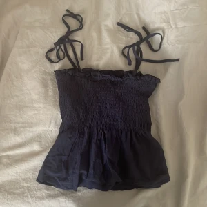 Marinblå topp med knytband och smock - Säljer denna jättegulliga topp med knytband då den tyvärr inte kommer till användning! Använd ett fåtal gånger, i storlek Xs💓