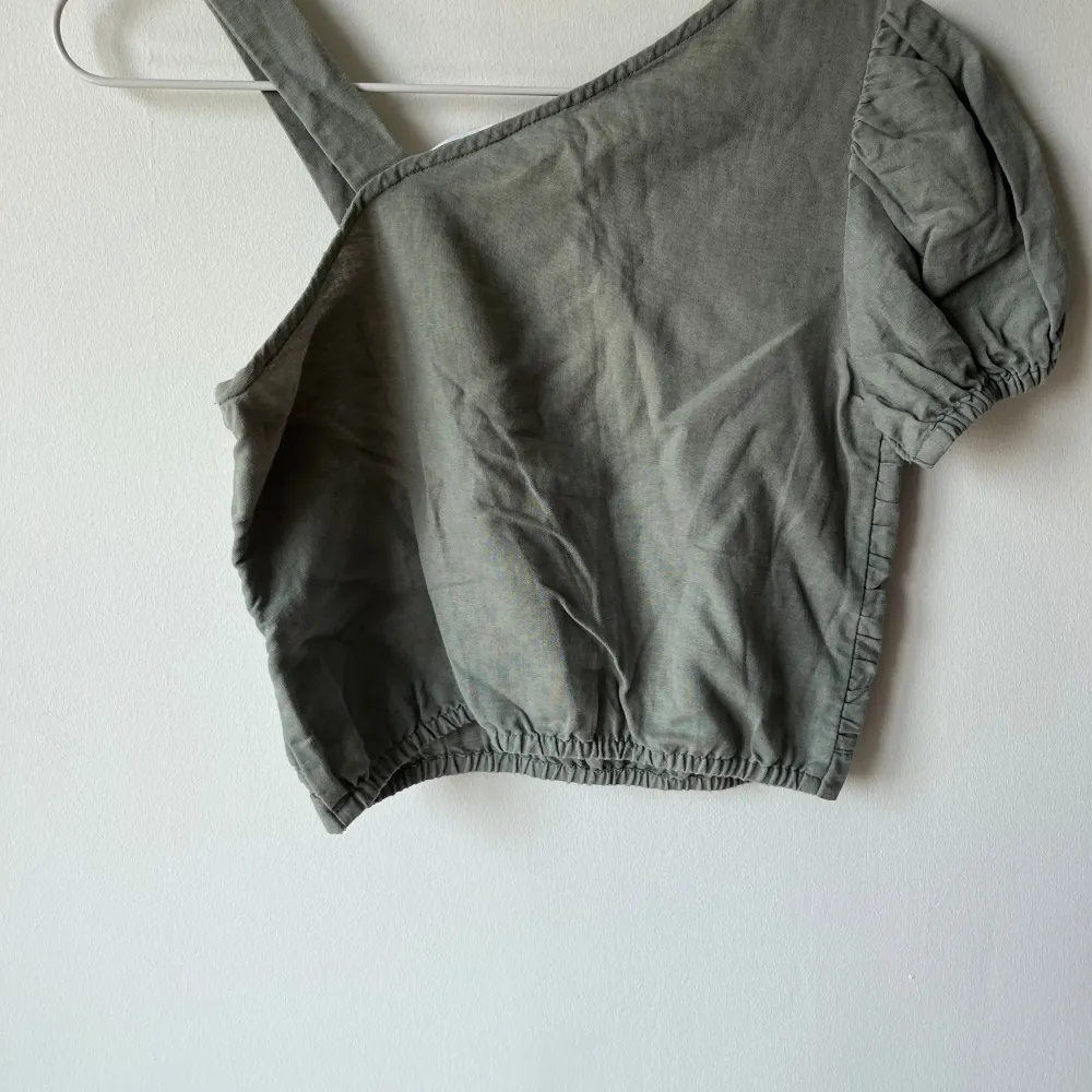 Säljer en snygg grön oneshoulder topp från Zara. Den har en cool knytdetalj framtill och puffiga korta ärmar. Perfekt för sommarens fester eller en dag på stan. Toppen är i bra skick och superbekväm att ha på sig!. Yläosat.