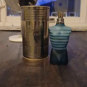 Säljer en ikonisk Jean Paul Gaultier Le Male Eau de Toilette. Flaskan är formad som en manlig torso i blått glas med ränder, vilket ger en cool och unik look. Parfymen kommer i en metallburk som ger en industriell känsla. Perfekt för den som vill ha en klassisk och maskulin doft.