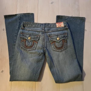 Lågmidjade True religon jeans - Snygga lågmidjade bootcut true religon jeans. Med lite lätta slitningar. Super coola sömmar i olika färger. W29 L32, dvs. S/M.