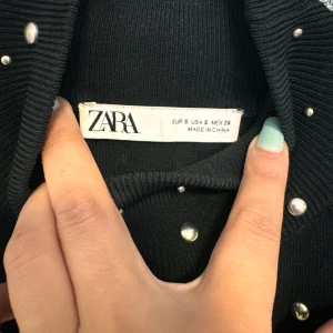 Svart ärmlös topp med pärlor från Zara - Säljer en snygg svart ärmlös topp från Zara. Den är dekorerad med små pärlor över hela framsidan vilket ger en glittrig och festlig look. Perfekt för en utekväll eller fest! Toppen är i storlek S och har en tight passform.