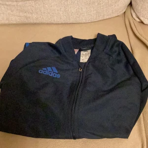 Mörkblå träningsjacka från Adidas - Säljer en snygg mörkblå träningsjacka från Adidas. Har bara använt den 2 gånger och är i bra skick. För er som vill ha översized frakten är inkluderar i priset!