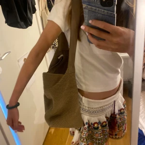 Beige stickad axelväska - Säljer en superfin beige stickad axelväska. Den är perfekt för vardagsbruk och har en snygg och enkel design. Väskan är rymlig och har en bekväm axelrem. Perfekt för sommarens alla äventyr!