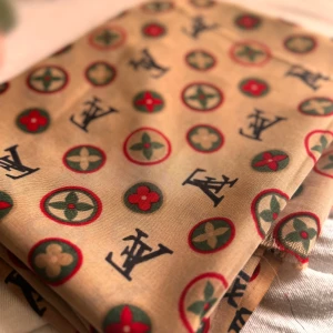 Beige halsduk med mönster - Säljer en superfin beige halsduk med ett coolt mönster i rött och grönt. Den har en lyxig känsla och är perfekt för att piffa upp vilken outfit som helst. Passar både till vardags och fest!