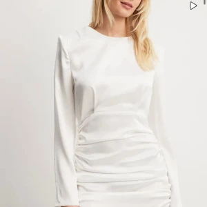 Vit långärmad klänning i satin - Säljer en elegant vit klänning i satin med långa ärmar. Klänningen har en tight passform och snygga rynkdetaljer längs sidorna som ger en smickrande siluett. Perfekt för festliga tillfällen eller en stilren look.