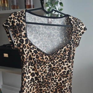 Leopardmönstrad topp med spetsdetaljer - Säljer en snygg leopardmönstrad topp med korta ärmar och v-ringning. Toppen har fina spetsdetaljer runt halsen som ger en extra touch. Perfekt för en utekväll eller fest!