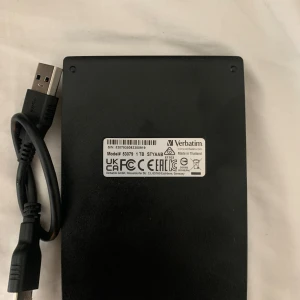 Extern hårddisk från Verbatim - Säljer en extern hårddisk från Verbatim med 1TB lagringsutrymme. Den är svart och kommer med en USB-kabel för enkel anslutning. Perfekt för att lagra stora mängder data eller säkerhetskopiera viktiga filer.