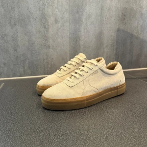 Beige sneakers från Axel Arigato - Säljer ett par stilrena beige sneakers från Axel Arigato. Skorna har en snygg och enkel design med en gummisula i en ljusbrun nyans. pris kan diskuteras!