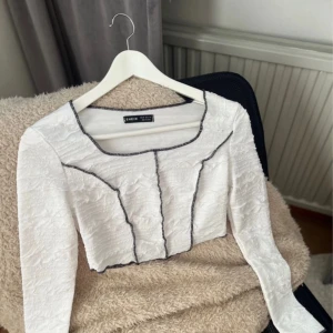 Vit topp från SHEIN - Säljer en snygg vit topp från SHEIN i storlek XS. Toppen har en unik design med svarta kontrastsömmar som ger den ett coolt utseende. Den är långärmad och perfekt för både vardag och fest. Materialet känns bekvämt och lätt att bära.