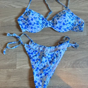 Blommig bikini i blått och vitt - Säljer en superfin bikini i storlek XL. Den är vit med blå blommor och har knytband på både över- och underdel. Överdelen har vadderade kupor och en praktisk spänne i ryggen. säljes billigt då knäppet är lite kärvt, men den är aldrig använd !
